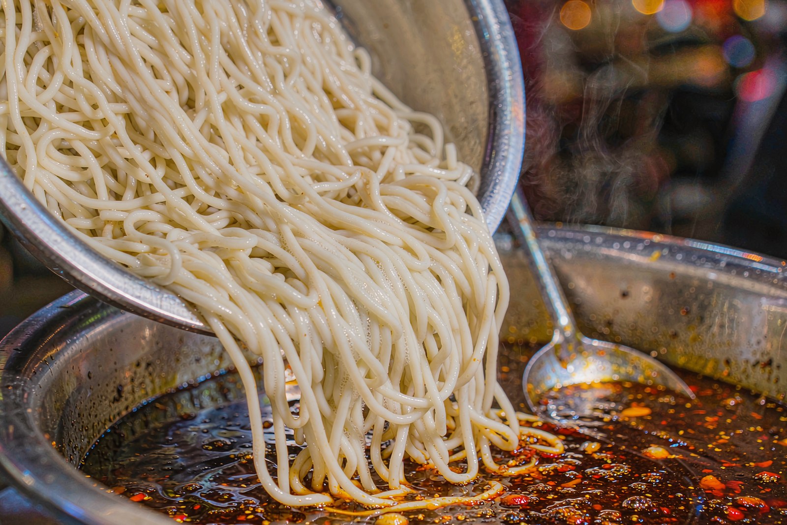 Plain boiled noodles being mixed into the last of the chilli sauce in the bottom of the basin