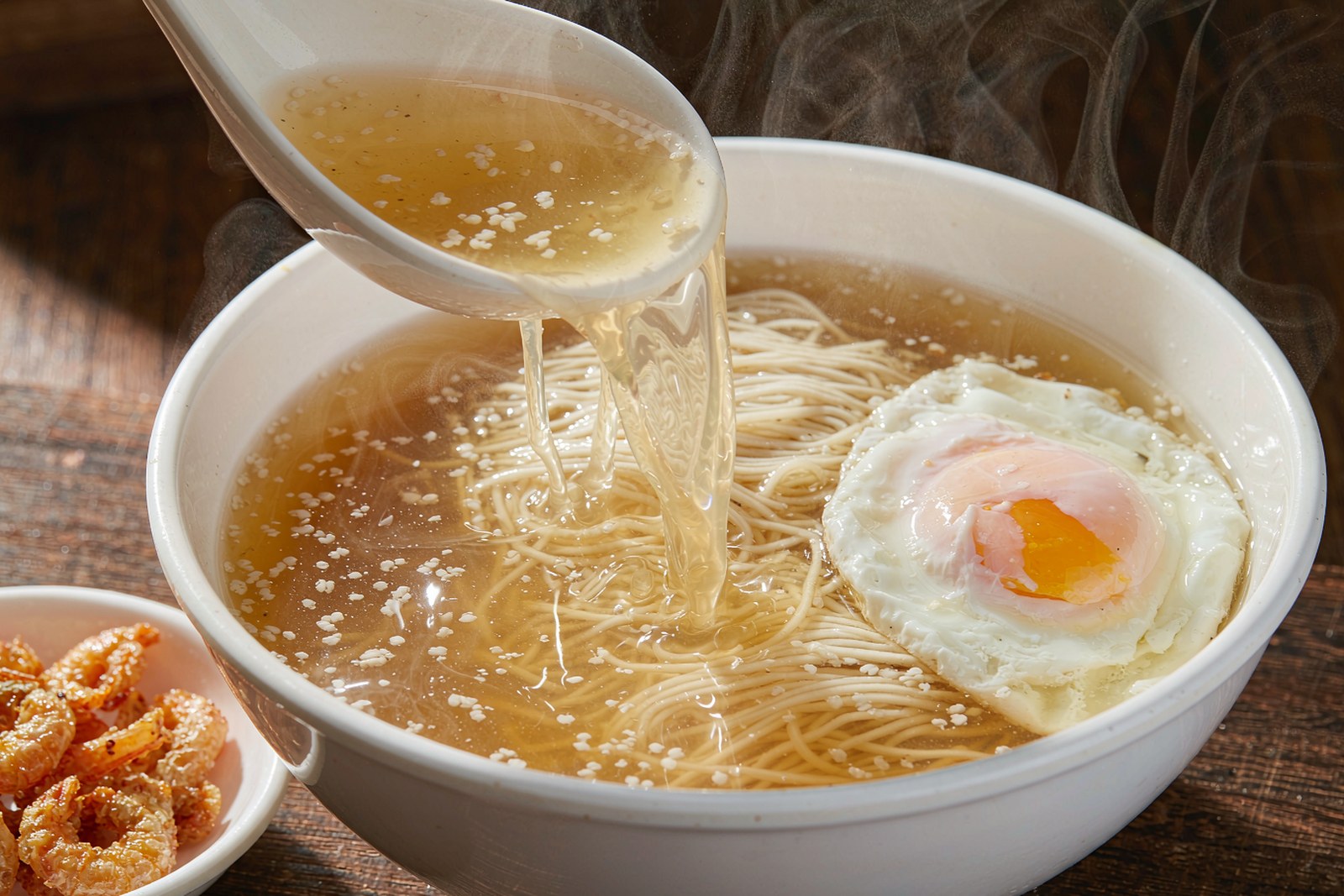A spoon lifting clear golden broth over Hou’an noodles