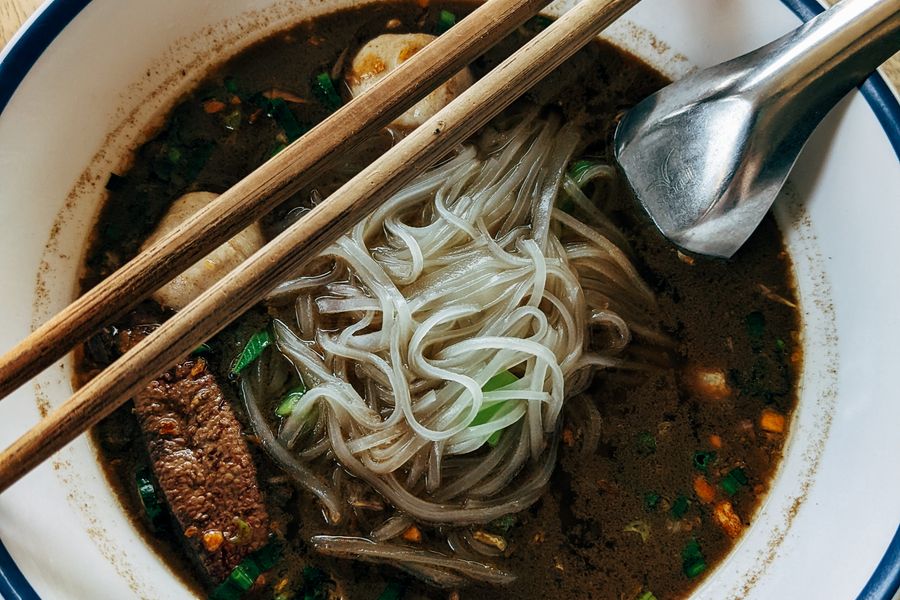 A busy noodle shop bowl with chili and toppings
