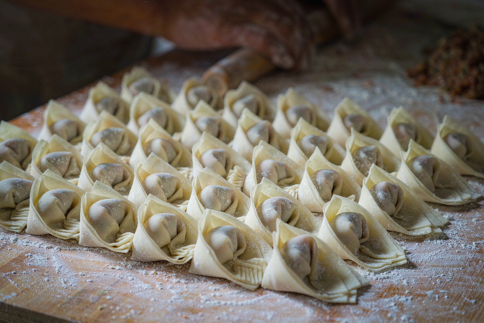 Folded wontons fanned out on a floured tray, ready for the pot
