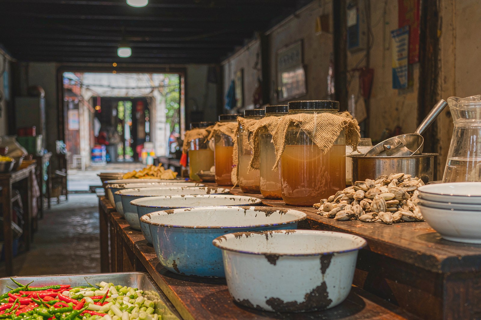 A row of enamel bowls on a shop counter with jars of cloudy rice vinegar behind