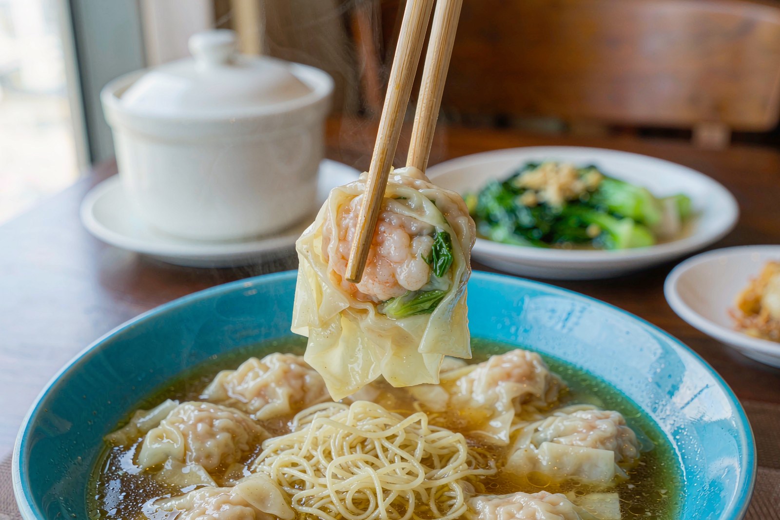 Chopsticks lifting a wonton with shrimp and noodles