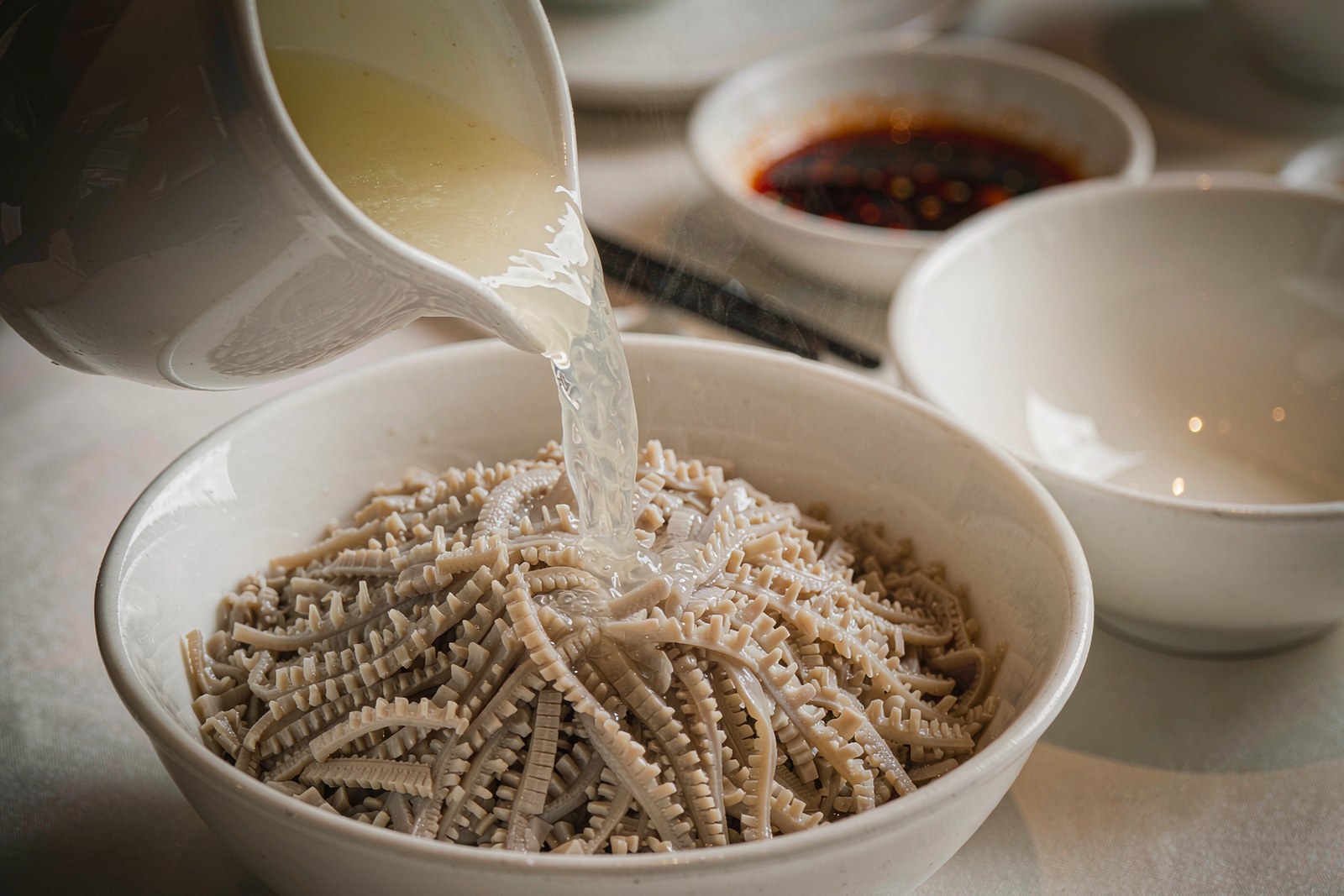 Clear stock poured from a jug over scored tripe tips in a white bowl