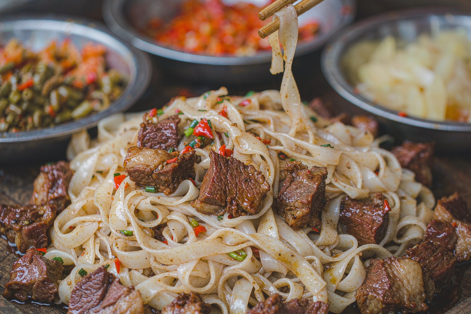Braised beef brisket over fresh flat rice noodles, with condiment trays behind
