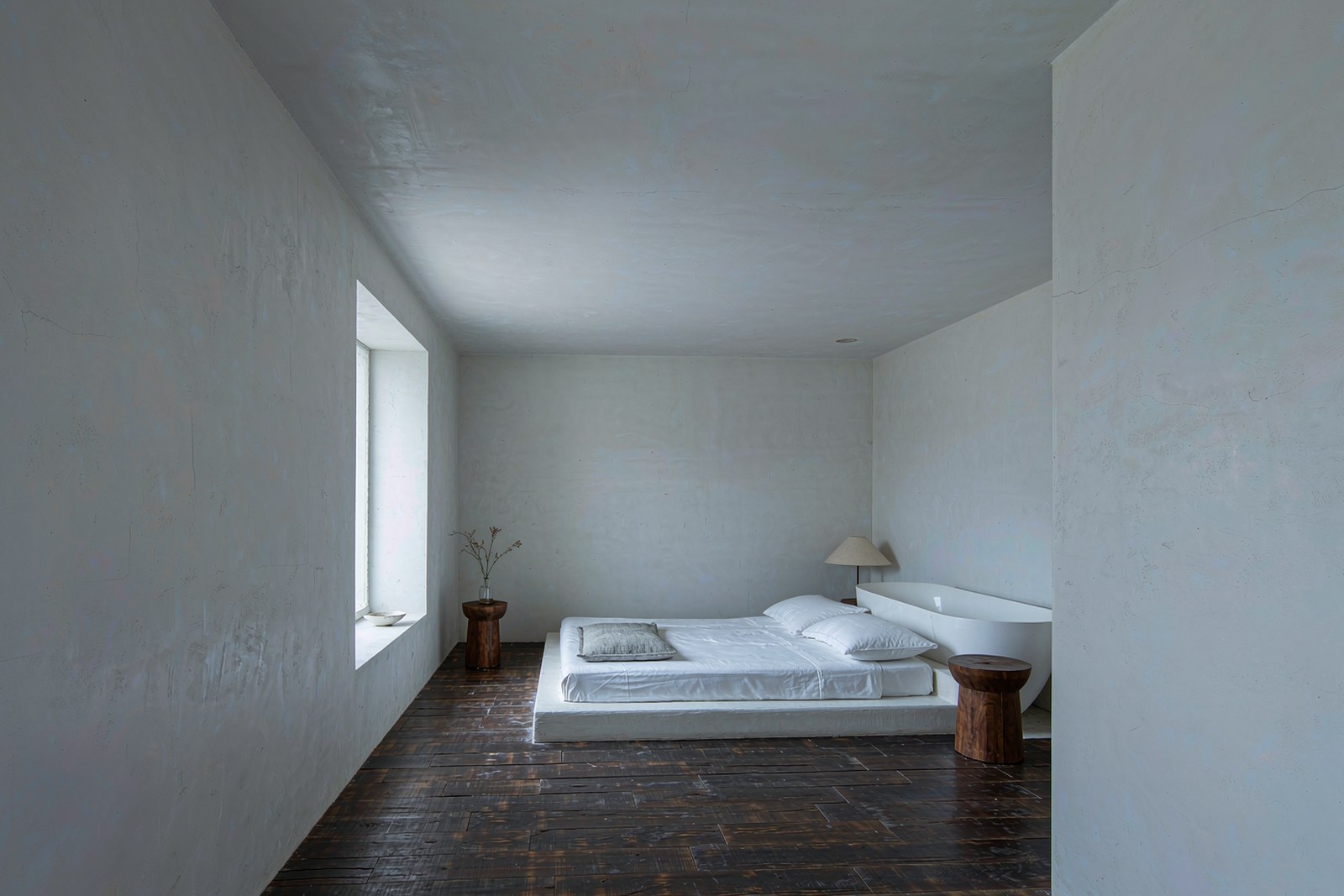 A minimal hotel room with pale walls, dark wood and a freestanding tub