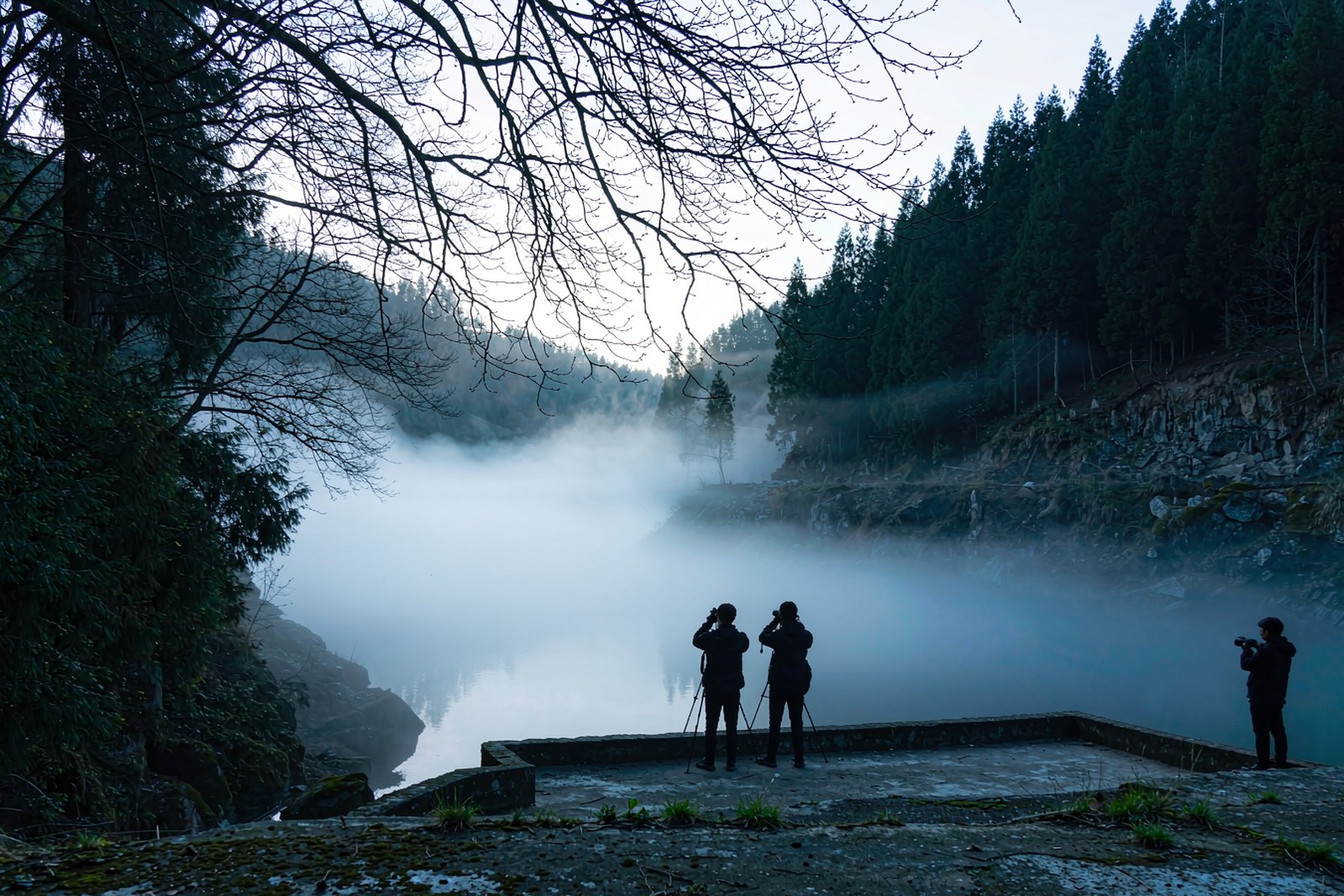 A stone viewing platform above a mist-covered river at dawn with photographers