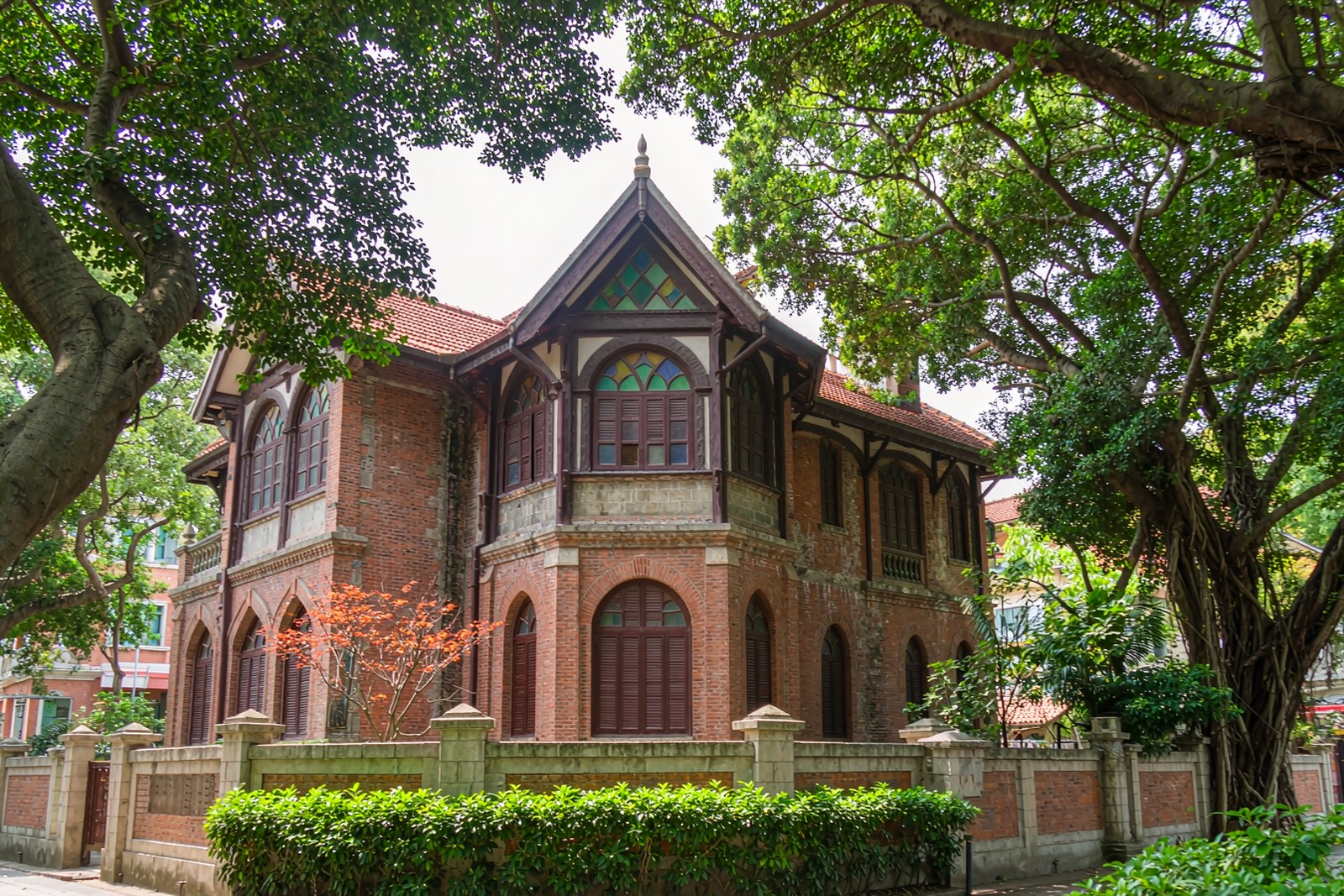 A red-brick villa with arched windows and a garden wall on a quiet lane