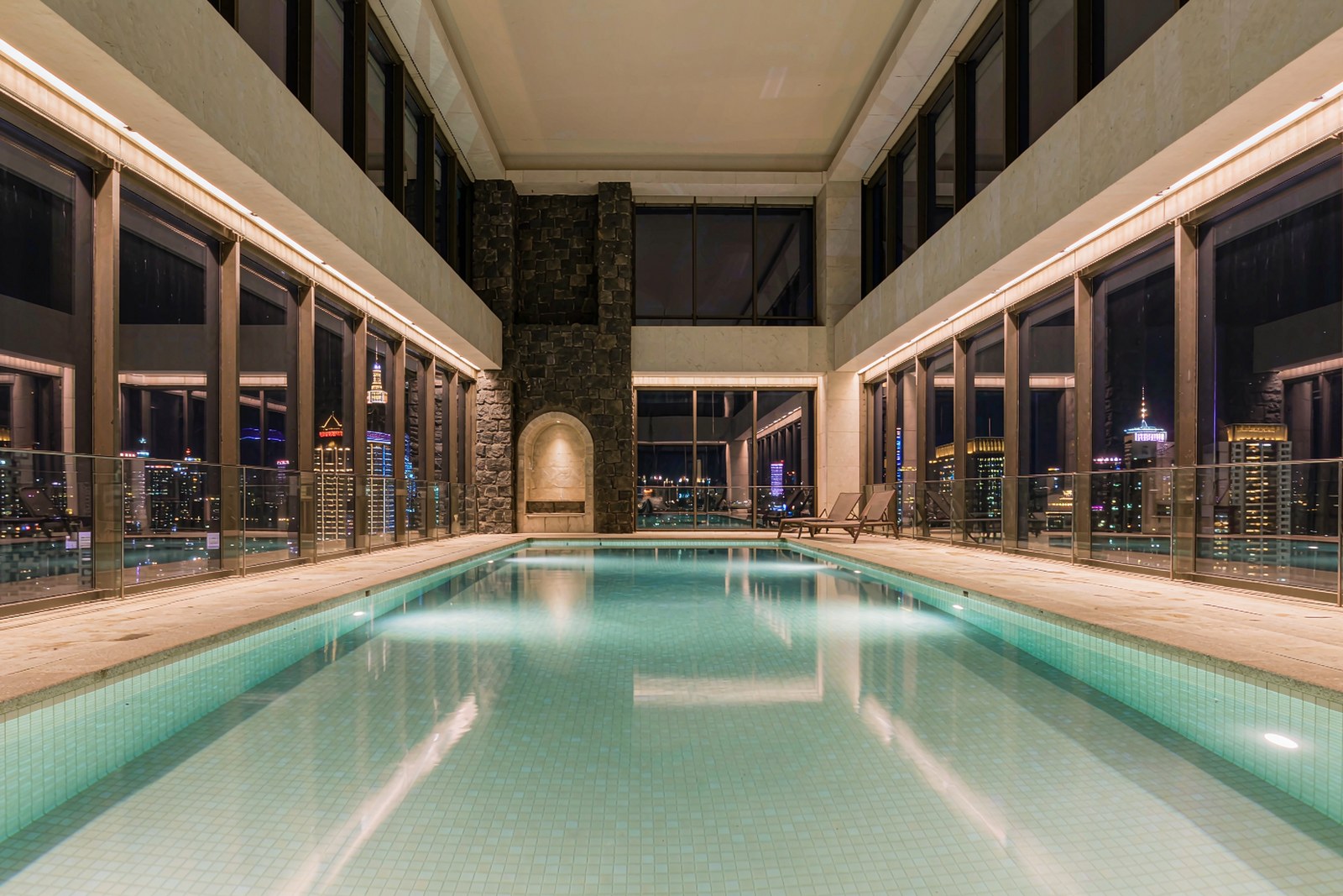 An indoor hotel pool at night, glass wall onto a lit city skyline
