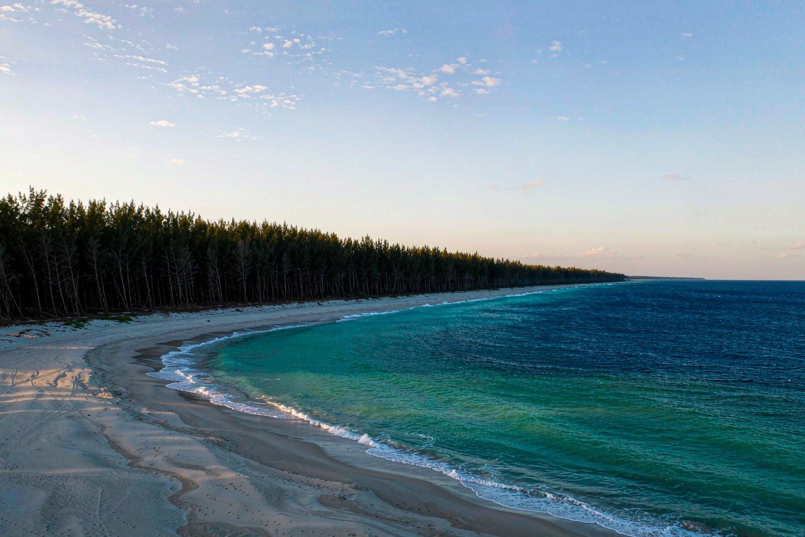 A long white crescent of beach backed by dark coastal forest at Shimei Bay