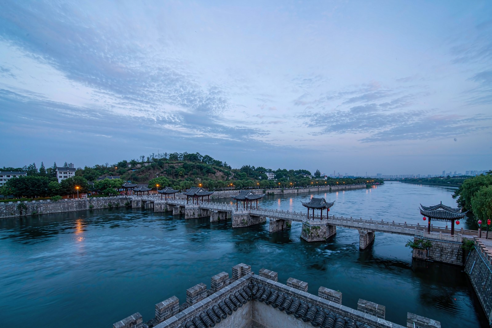 Stone piers with pavilions on an ancient bridge over a wide river, seen from a gate tower