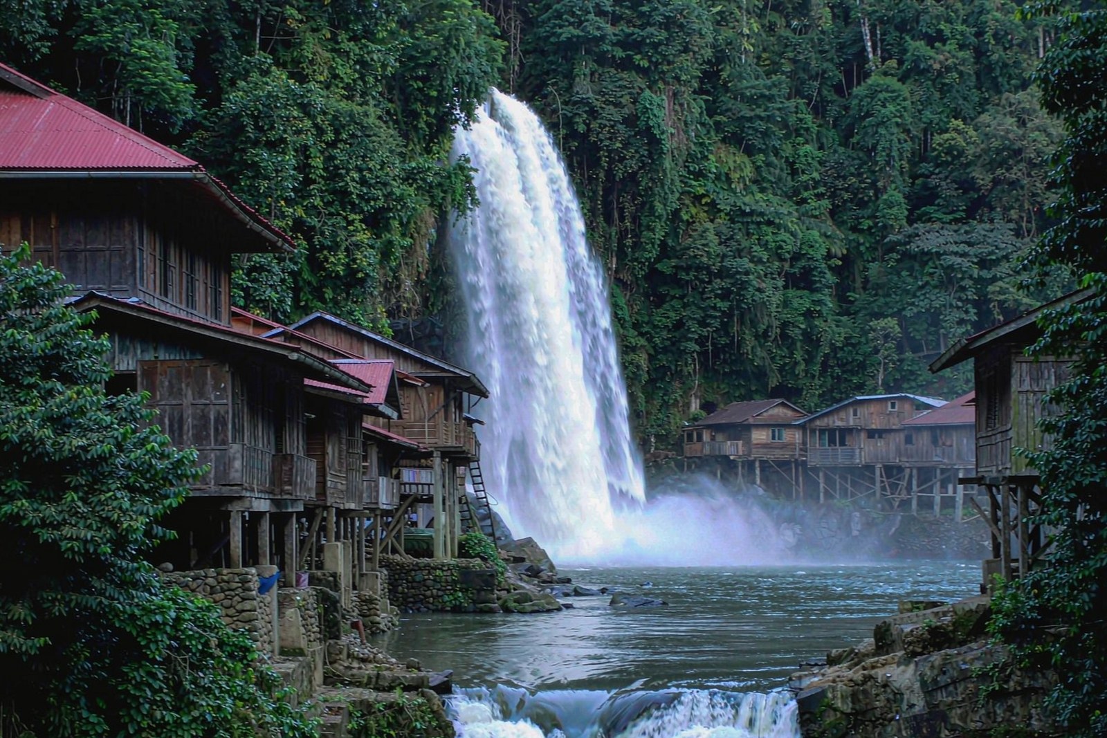 A tall waterfall falling through a riverside town with timber houses on both banks