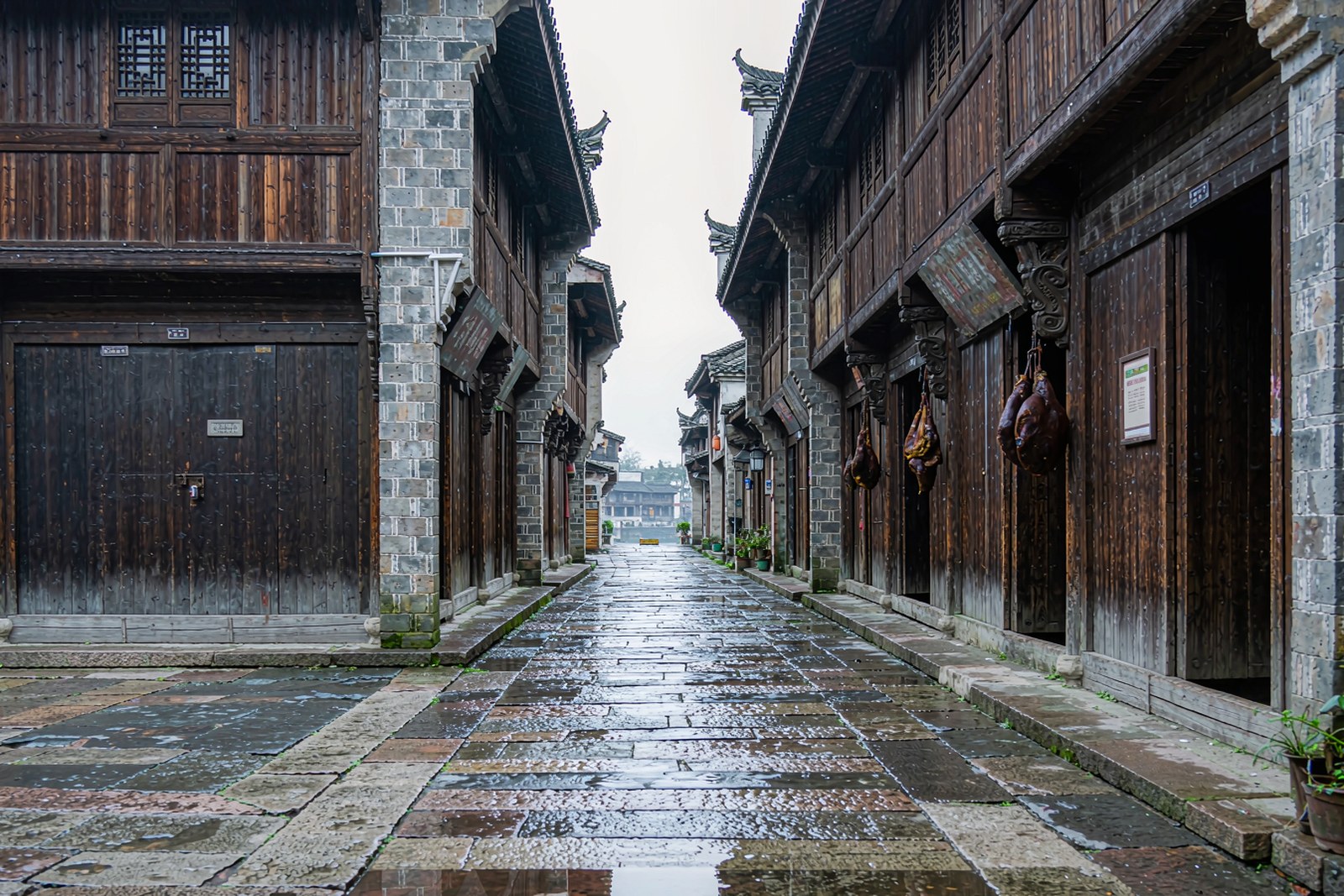A narrow stone-slab street lined with timber shops and hanging cured meat