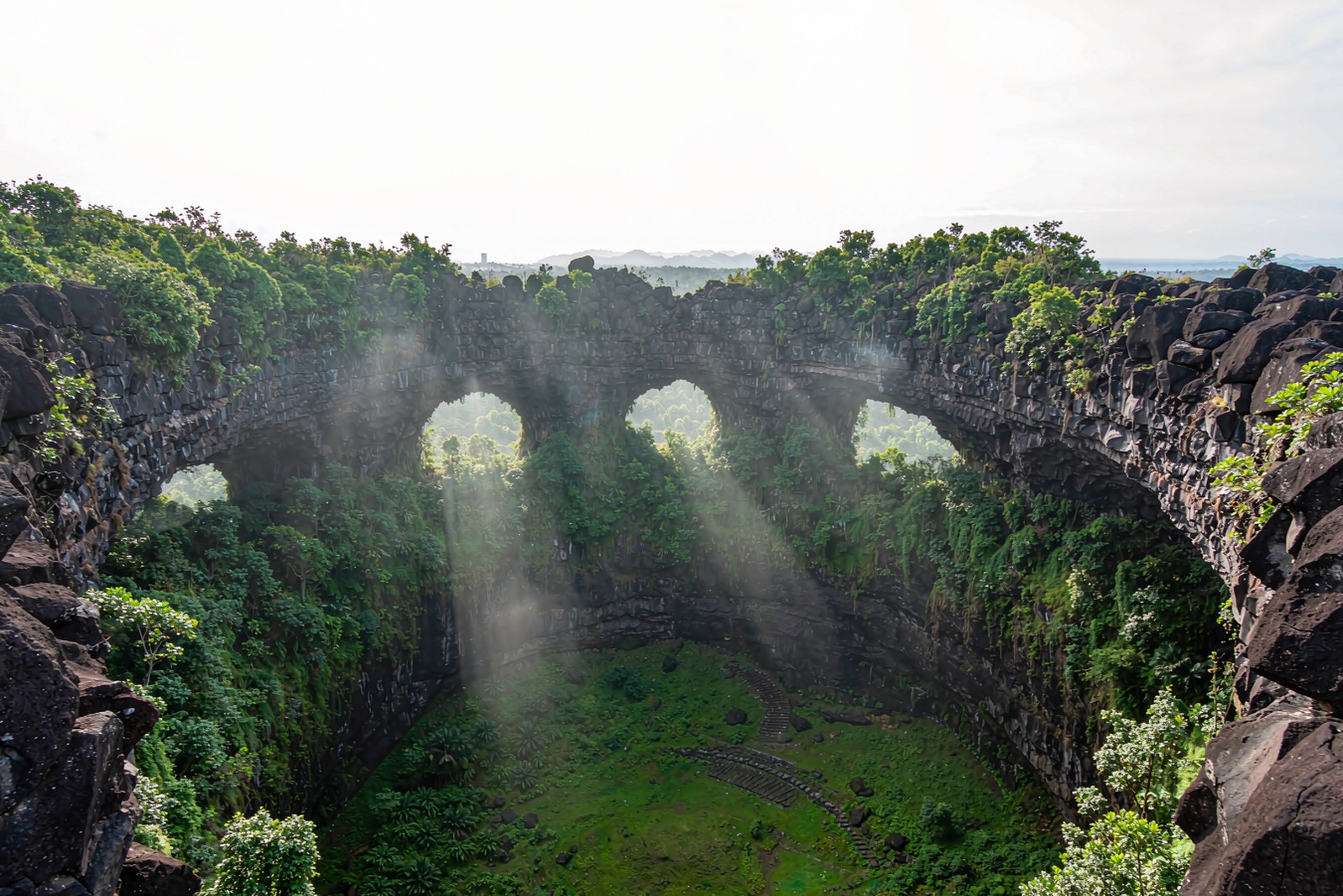 A round volcanic crater with black basalt walls and green tropical vegetation